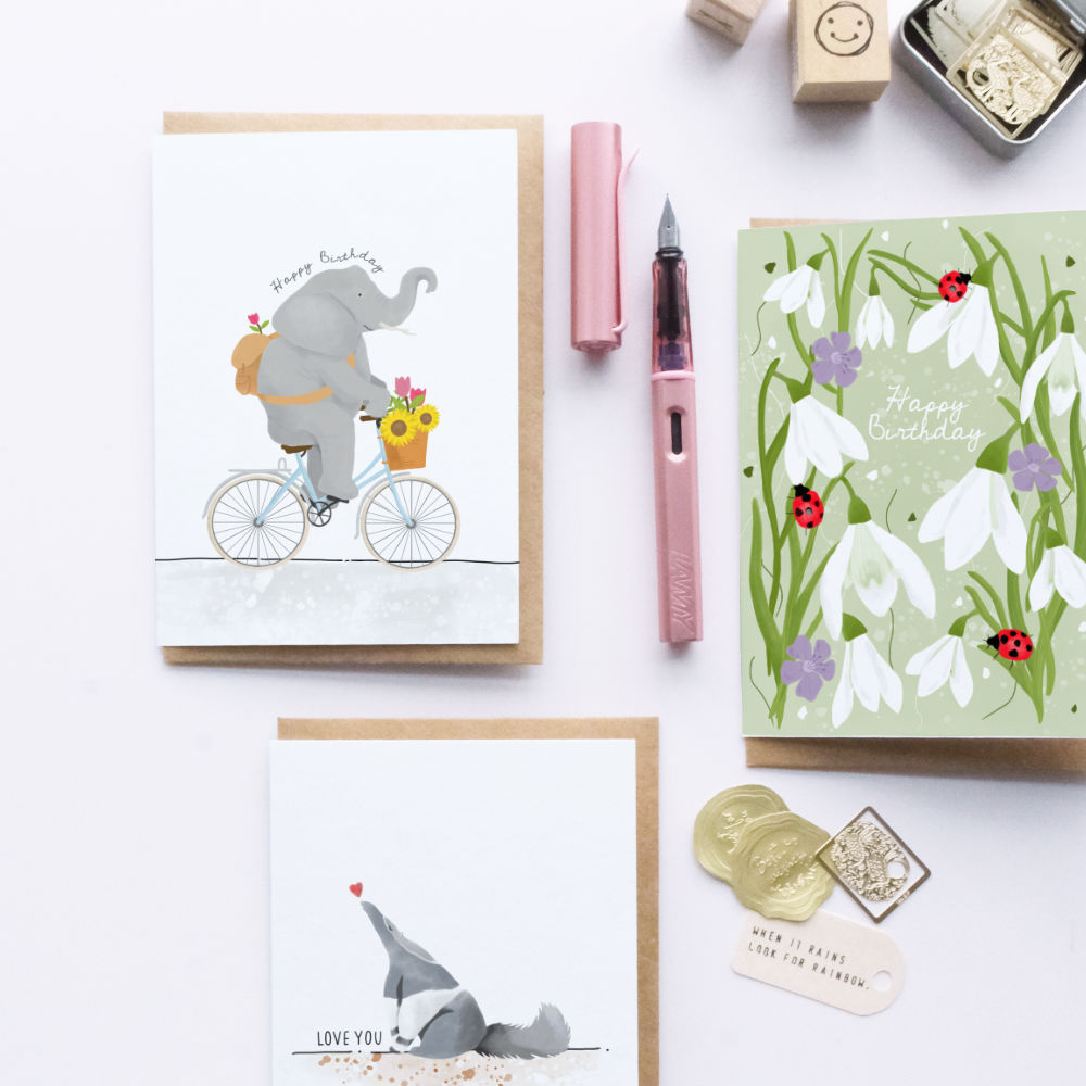 Collection of greeting cards with illustrations on a white surface with stationery items.