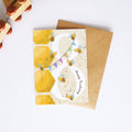 A honey-themed birthday card with a large white number 8 decorated with yellow honeycombs, bumblebees, and the words 'Happy Birthday', shown with a brown kraft envelope on a white background.