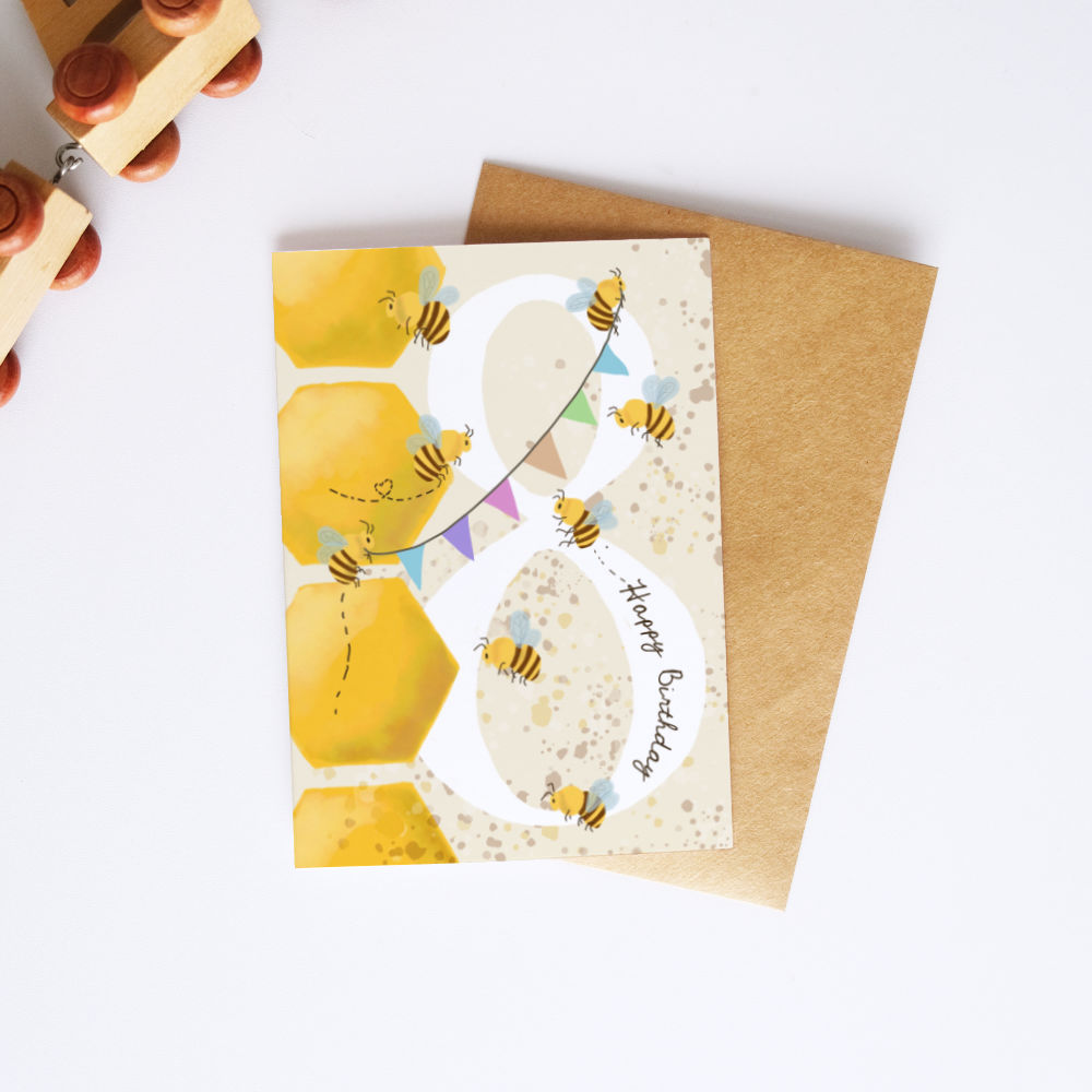 A honey-themed birthday card with a large white number 8 decorated with yellow honeycombs, bumblebees, and the words 'Happy Birthday', shown with a brown kraft envelope on a white background.