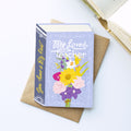 A book-shaped card  titled "My Beloved Teacher" with a lavender cover and colourful flower illustration, placed on top of a brown envelope. The spine reads "You have a Big Heart" .