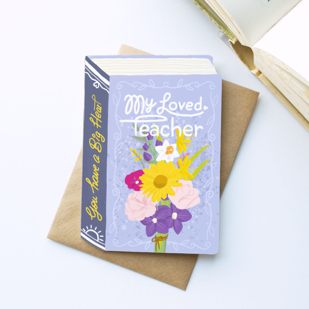 A book-shaped card  titled "My Beloved Teacher" with a lavender cover and colourful flower illustration, placed on top of a brown envelope. The spine reads "You have a Big Heart" .