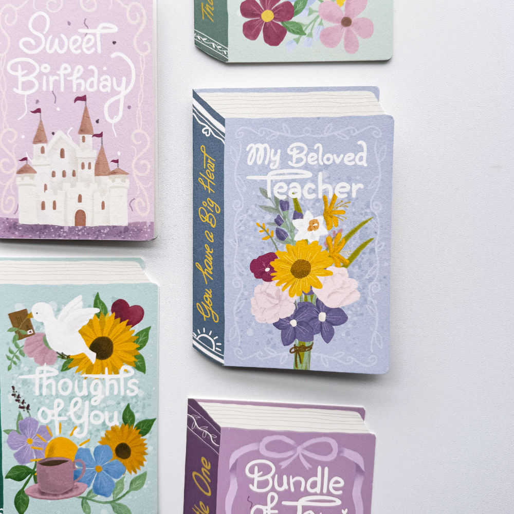 A set of decorative book-shaped greeting cards or keepsake books arranged on a white background. Visible designs include a lavender castle card reading 'Sweet Birthday,' a light blue card reading 'My Beloved Teacher' with a flower bouquet, a teal card with sunflowers and a dove reading 'thoughts of you,' and a purple card reading 'Bundle of.